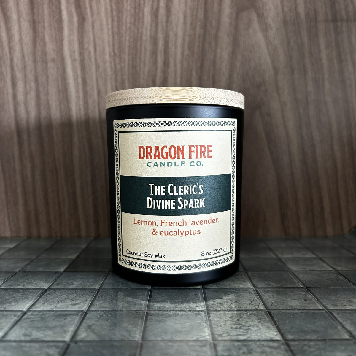 A Dragon Fire Candle Co. coconut soy wax candle in a black glass jar with a bamboo lid, featuring a cream and dark green label that reads 'The Cleric's Divine Spark'.